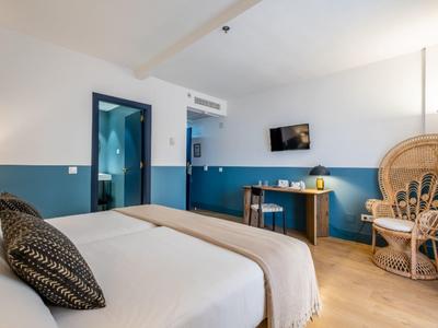 Modernes Hotelzimmer mit Doppelbett, blauer Wandverzierung, Fernseher und Korbsessel mit Lampe.