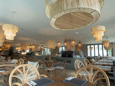 Helles Restaurant mit Holzstühlen, großen Lampen und eingedeckten Tischen mit Blick auf Fenster.