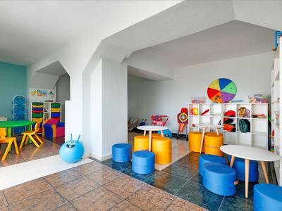 Bunter Kinderspielraum mit Tischen, Stühlen und buntem Lernrad in einem hellen Raum.