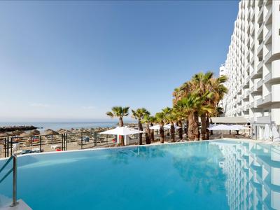 Moderner Außenpool mit Blick auf das Meer an einem Hotel bei klarem Himmel.
