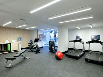 Moderner Fitnessraum mit Laufbändern, Hantelbänken und großen Fenstern in einem Hotel.