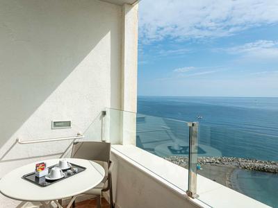 Balkon mit kleinem runden Tisch, Stuhl und Meerblick unter blauem Himmel mit Wolken.