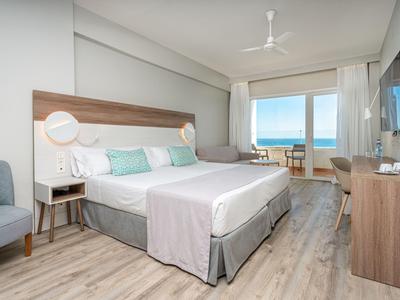 Modernes Hotelzimmer mit Doppelbett und Meerblick durch bodentiefe Fenster.