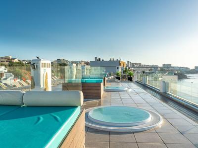 Dachterrasse mit Pool, Whirlpool und Liegen mit Meerblick bei klarem Himmel.