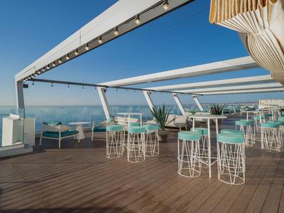 Freiluft-Dachterrasse mit modernen Tischen und hohen Stühlen, mit Meerblick.