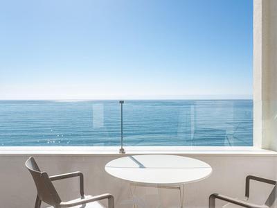 Balkon mit Tisch und Stühlen mit Blick auf ruhiges, blaues Meer unter klarem Himmel.