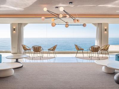 Moderne Hotel-Lounge mit Meerblick, blauen Sofas und runden weißen Tischen.