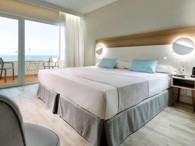 Modernes Hotelzimmer mit Doppelbett, Balkon, Meerblick, hellen Wänden und minimalistischer Einrichtung.