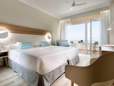 Modernes Hotelzimmer mit zwei Betten, Balkon, Sitzbereich und Meerblick bei Tageslicht.