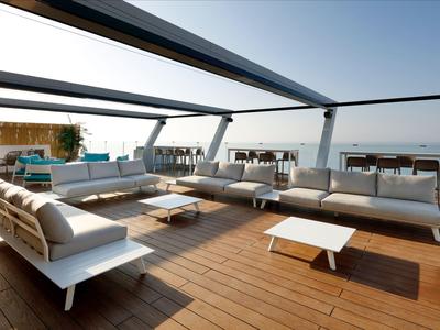 Moderne Dachterrasse mit weißen Loungemöbeln und Holzfußboden, Meer im Hintergrund.