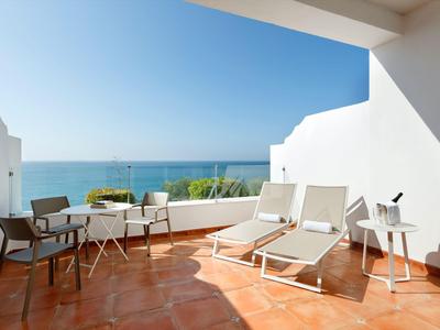 Terrasse mit Liegestühlen und Stühlen mit Meerblick bei sonnigem Wetter.