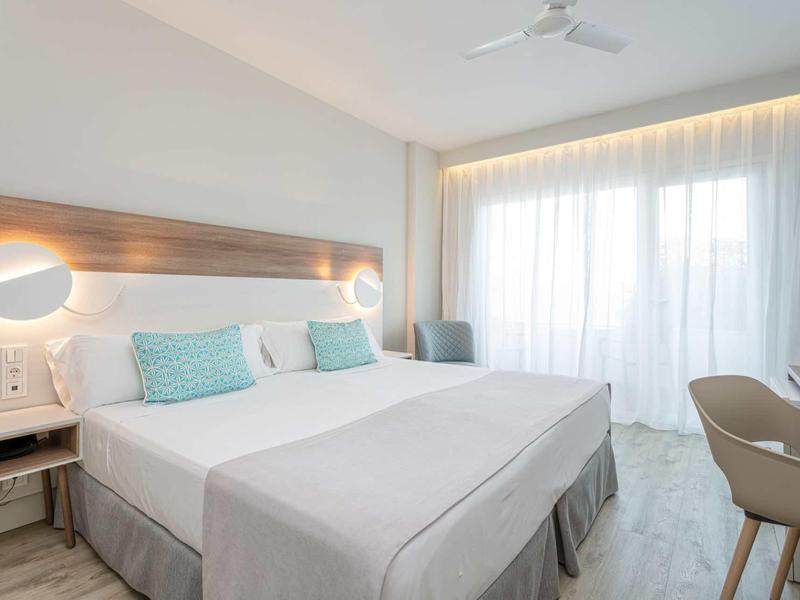 Modernes Hotelzimmer mit zwei Einzelbetten, hellen Wänden, Vorhängen und dezentem Holzmobiliar.