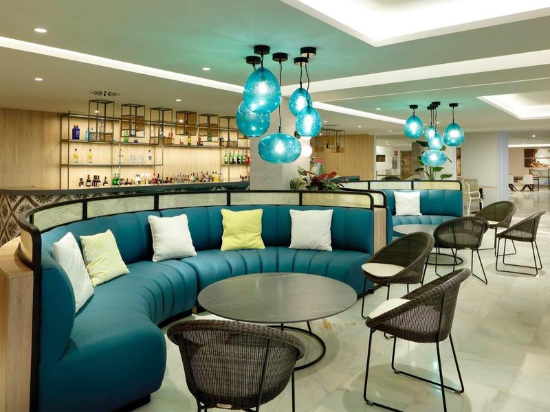 Moderner Lounge-Bereich mit blauem Rundsofa, runden schwarzen Tischen und hellblau leuchtenden Lampen.