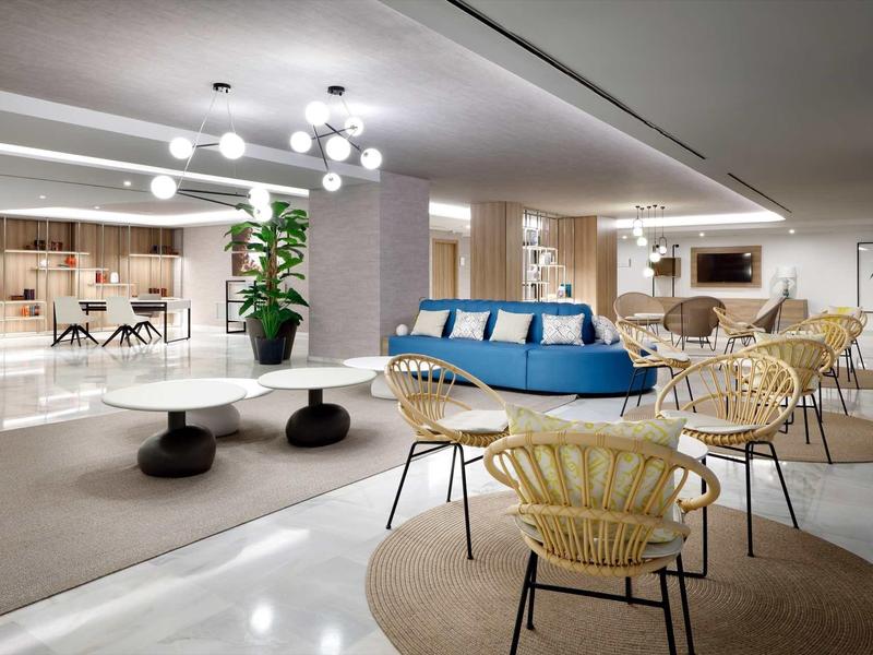 Moderner, heller Aufenthaltsbereich mit blauen Sofa, runden Tischen und Stühlen auf Teppichboden.