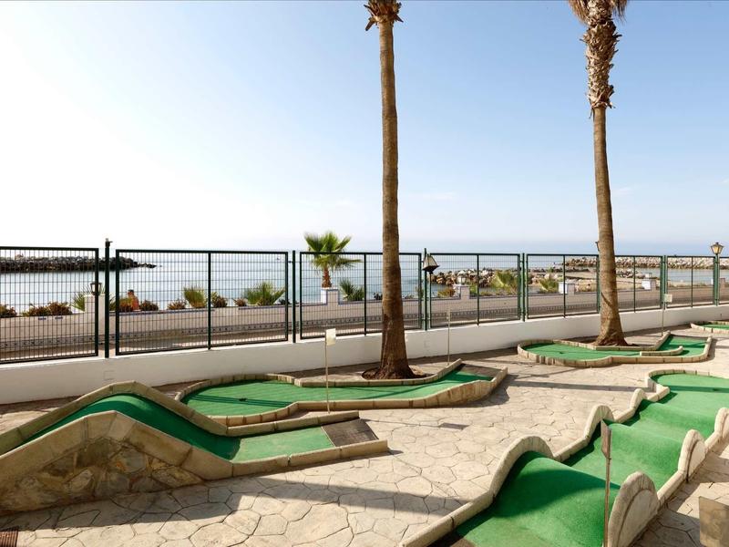 Minigolfplatz mit grünem Kunstrasen, Palmen und Meerblick im Hintergrund an sonnigem Tag.