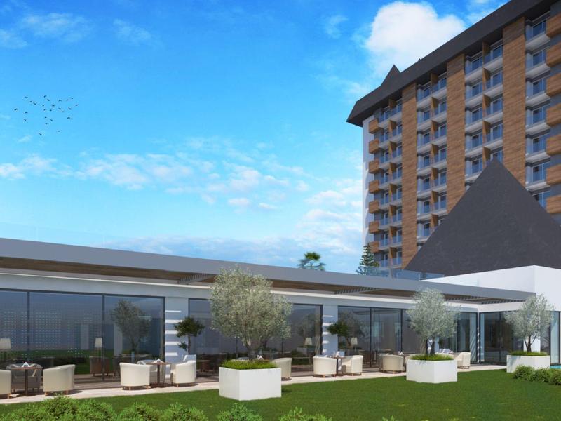 Moderner Gebäudekomplex mit Glasfront, Terrasse und Hochhaus unter blauem Himmel.