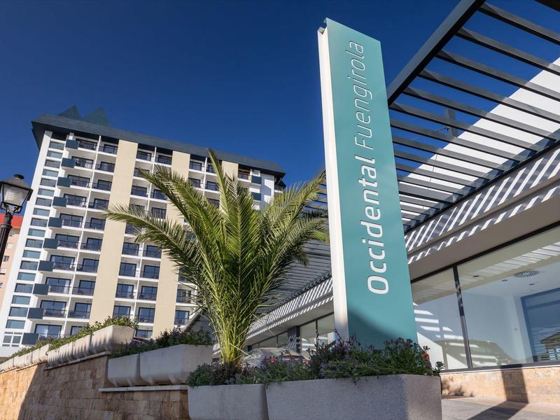 Moderner Gebäudekomplex mit Palmen und blauem Himmel, Schild zeigt "Occidental Luz Bonita" an.