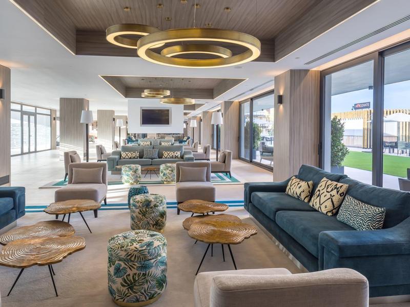 Moderner Wohnraum mit blauen Sofas, runden Couchtischen, Hockern und großen Fenstern zum Garten.