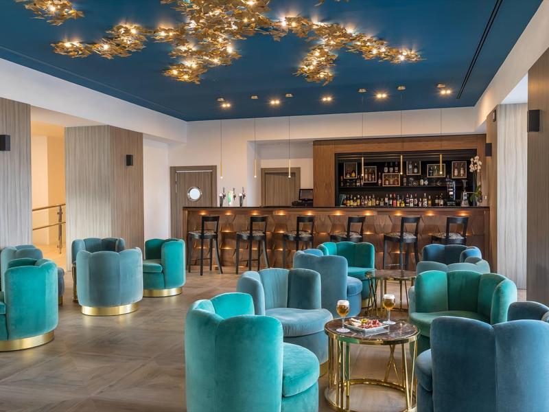 Moderner Barraum mit smaragdgrünen Sesseln, Holzbar und dekorativer Deckenbeleuchtung.