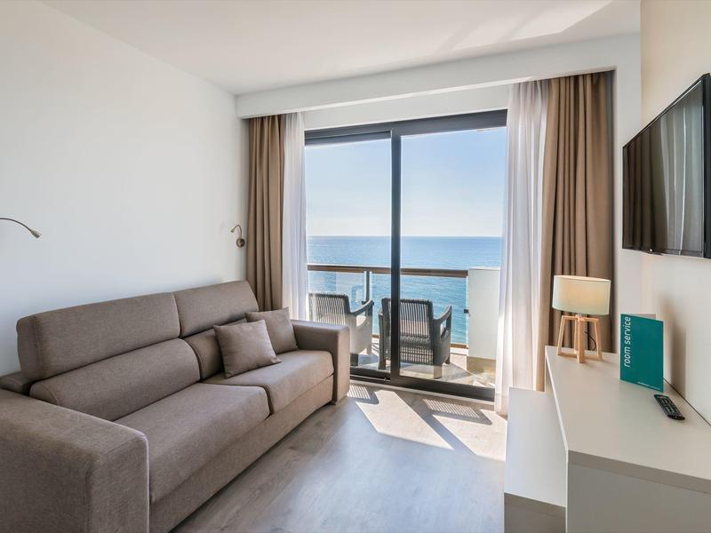 Helles Wohnzimmer mit grauem Sofa, großem Fenster und Balkon mit Meerblick.