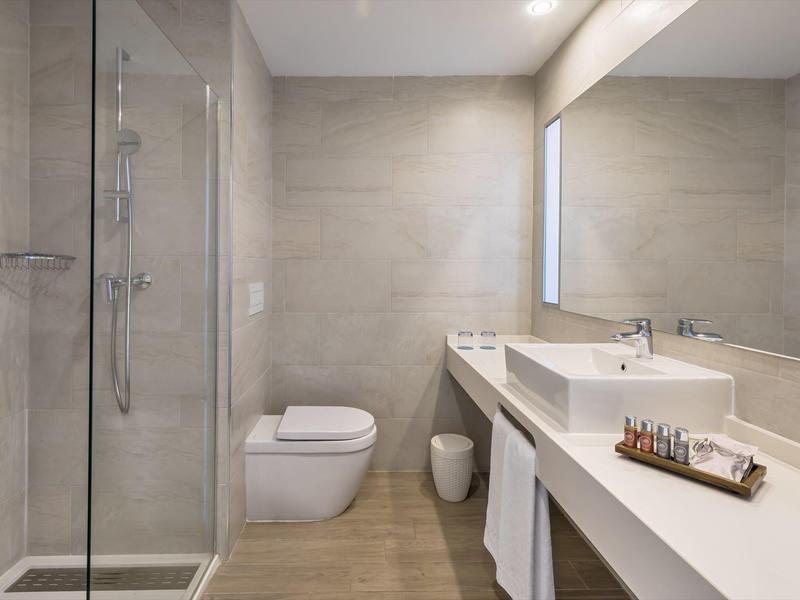 Modernes Badezimmer mit Glas-Dusche, wandhängendem WC, großem Spiegel und weißem Waschbecken.