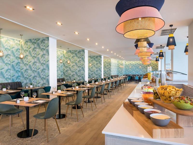 Moderner, heller Speisesaal mit langen Reihen von Tischen, stilvollen Stühlen und Dekolampen.