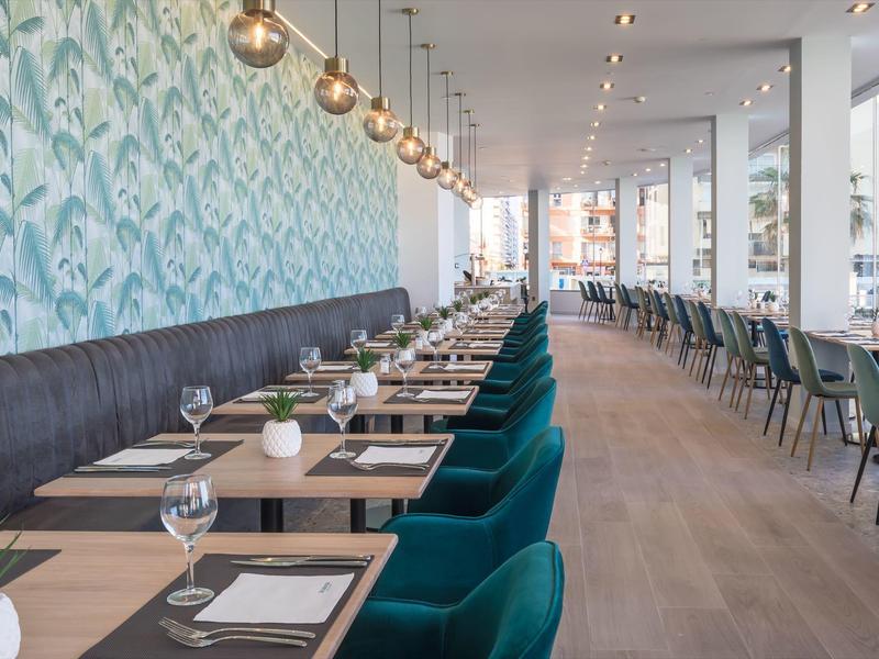 Moderner Restaurantinnenraum mit blauer Wand, dunklen Stühlen, Holzboden und eleganter Beleuchtung.