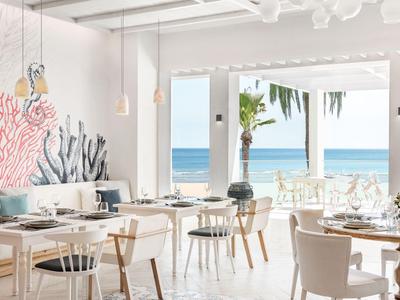 Modernes, helles Hotelrestaurant mit Meerblick, minimalistischer Einrichtung und maritimen Wanddekorationen.