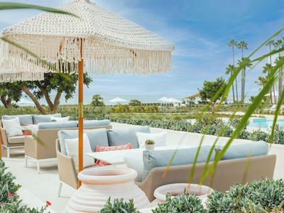 Moderne Außenterrasse mit Sofas und Sonnenschirmen neben einem Pool in einer Hotelanlage.