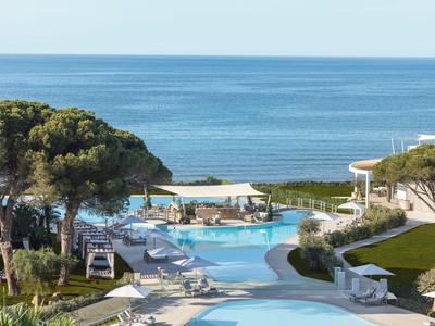 Hotelpool mit Liegestühlen und Blick auf das blaue Meer und den klaren Himmel.