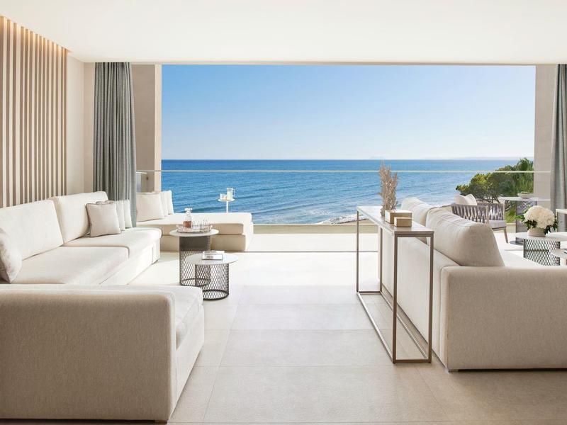 Helles Wohnzimmer mit weißen Sofas, großem Fenster und Meerblick bei klarem Wetter.