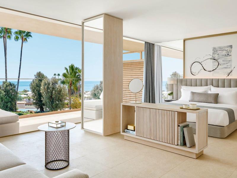 Helles Hotelzimmer mit großen Fensterfronten, Meerblick, hellen Holzmöbeln und modernen Möbeln.