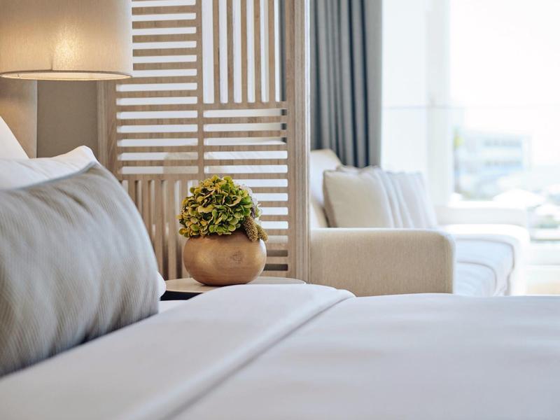 Weißes Bett mit grauem Kissen, Holzdeko und verziertem Raumteiler im hellen, modernen Zimmer.