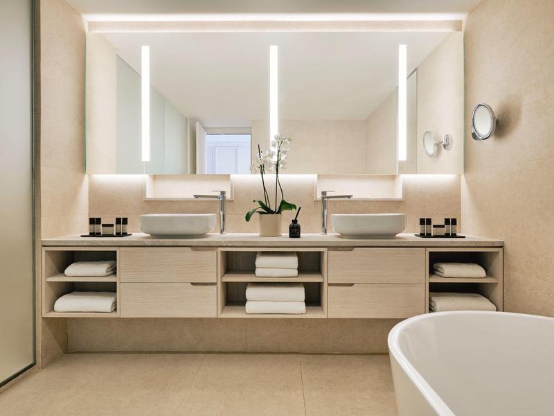 Modernes Badezimmer mit Doppelwaschbecken, großen Spiegeln, weißen Handtüchern und freistehender Badewanne.