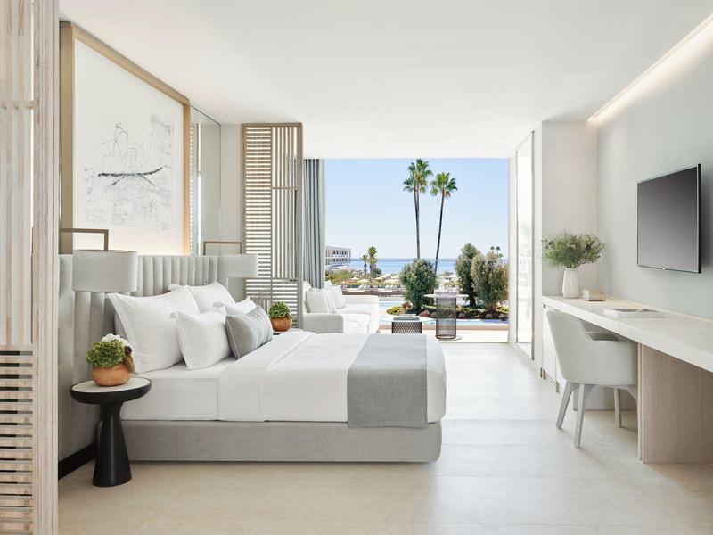 Helles, modernes Schlafzimmer mit Doppelbett, weißer Einrichtung und Blick auf Palme und Meer.