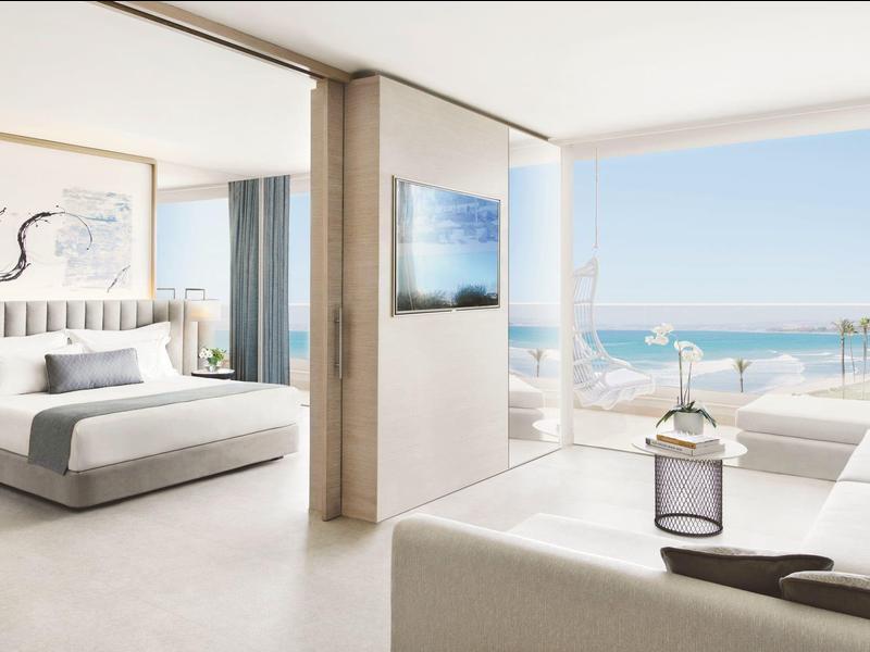 Helles modernes Schlafzimmer mit großem Fenster, Blick aufs Meer, weißes Bett und minimalistischer Deko.