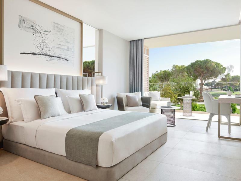 Helles Schlafzimmer mit großem Bett, Sofa, Schreibtisch und offener Terrasse mit Grünblick.