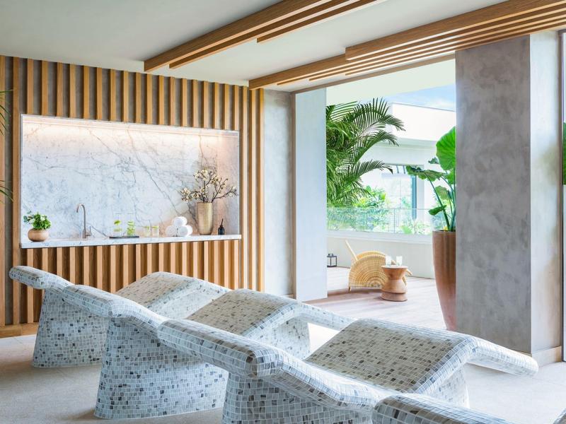 Moderne Terrasse mit grauen, gepunkteten Liegen, Holzwand und großen Pflanzen im hellen Raum.