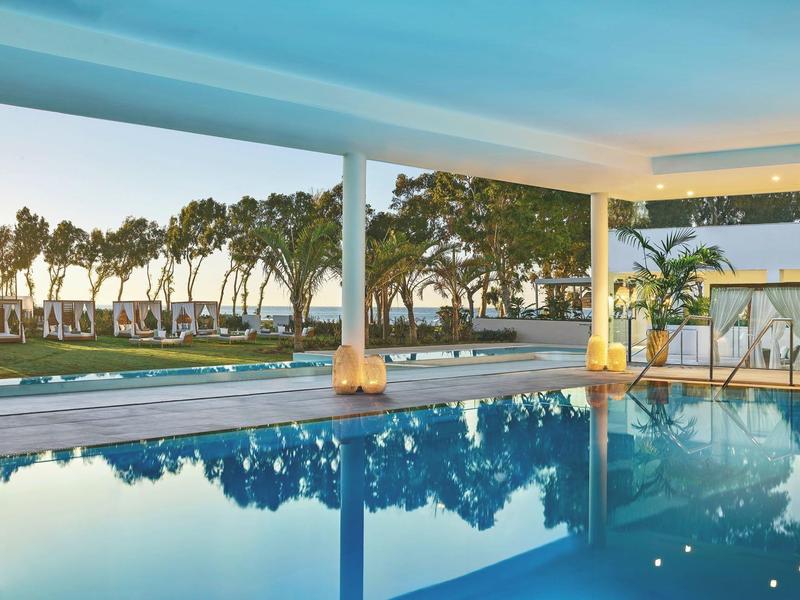 Moderner Außenpool mit klarem Wasser, Säulen und Blick auf Bäume bei blauem Himmel.