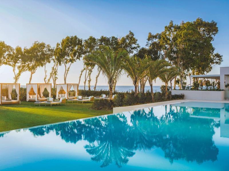 Großer blauer Pool mit grünem Rasen, Bäumen und Stühlen unter blauem Himmel.