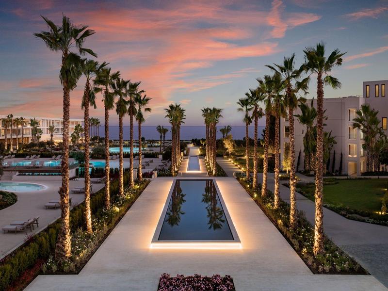 Symmetrischer Garten mit beleuchteten Palmen, Wasserbecken und buntem Sonnenuntergangshimmel.