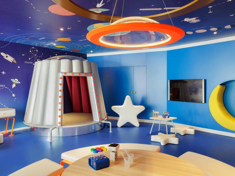 Bunter Kinderraum mit Weltraumwandgestaltung, Zelt, Stern- und Mondsitz, Tischen und Spielzeug.