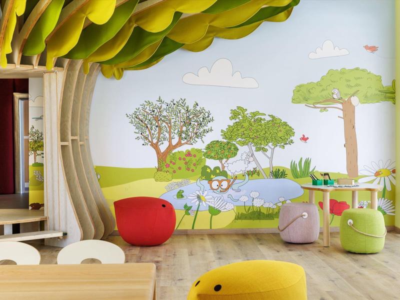 Bunter Kinderspielraum mit Baum-Wandgestaltung, weichen Sitzsäcken und hellem Holzboden.