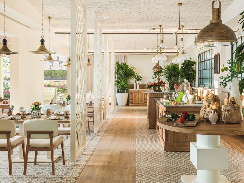 Hell gestalteter, moderner Speiseraum mit Holz- und Weißtönen, Pflanzen und großer Fensterfront.