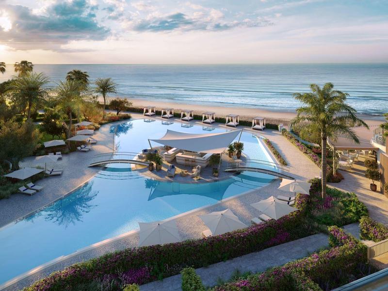 Großer Pool mit Inselbar, umgeben von Sonnenschirmen, Palmen und Blick auf das Meer.