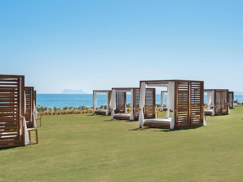 Grüne Wiese mit mehreren Holzbettgestellen, blauer Himmel und Meer im Hintergrund.
