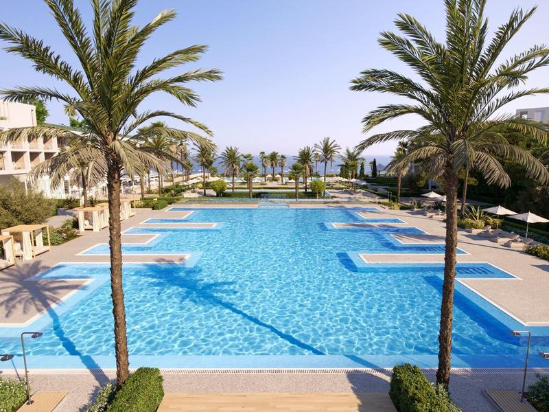 Großer blauer Pool mit Palmen, weißen Gebäuden und Liegestühlen unter klarem Himmel.