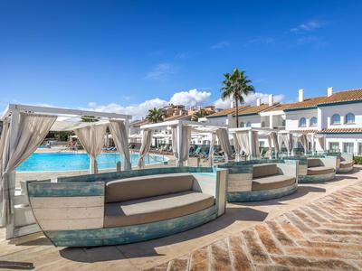 Luxuriöse Poolliegen mit weißen Vorhängen an einem großen, blauen Hotelpool unter blauem Himmel.