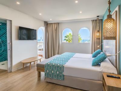 Modernes Schlafzimmer mit Doppelbett, hellen Holzböden, großen Fenstern und türkisen Akzenten.