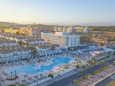 Große Hotelanlage mit Pool, weißen Gebäuden, roten Dächern und umliegenden Straßen bei Sonnenuntergang.